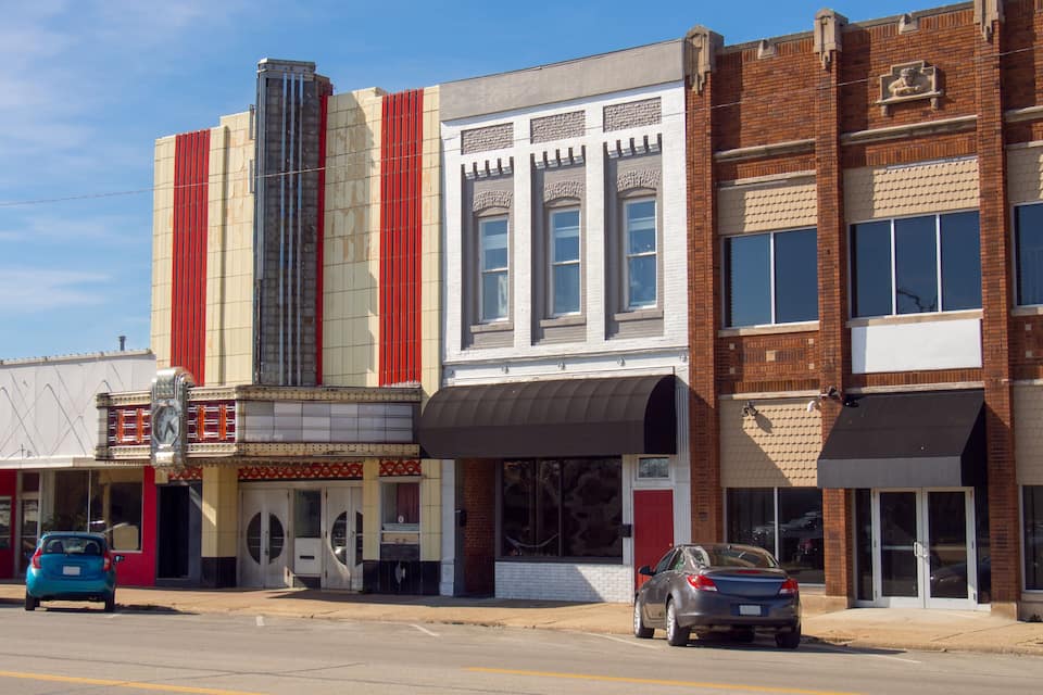 A street with a theater, a brick building, and parked cars.