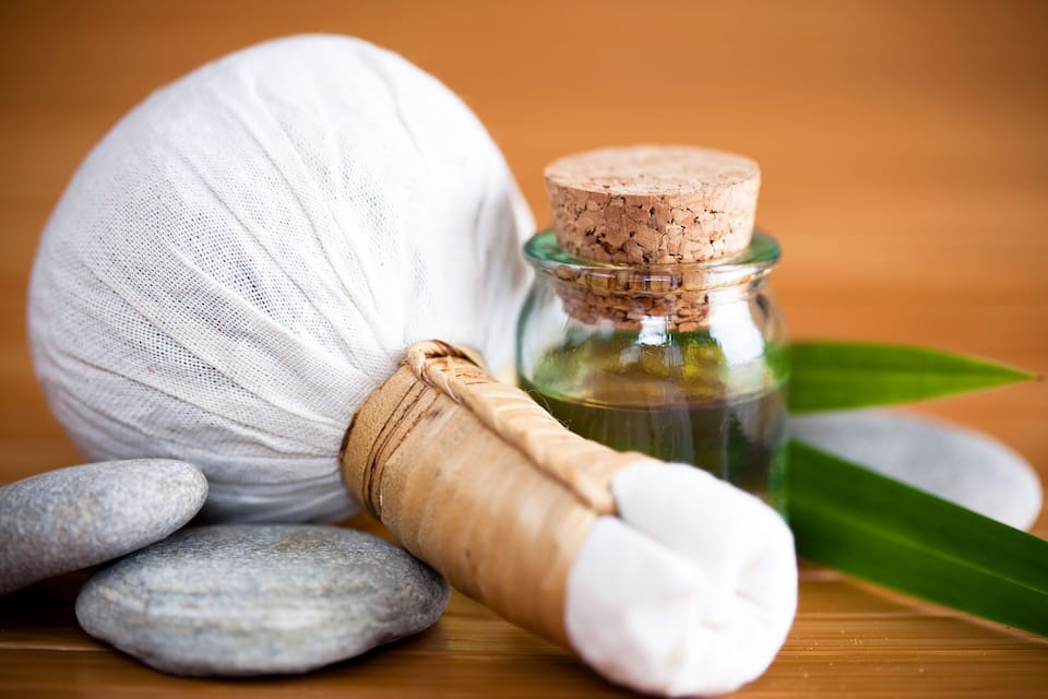 A massage stone, a bottle with cork stopper, and a green leaf on a wooden surface.
