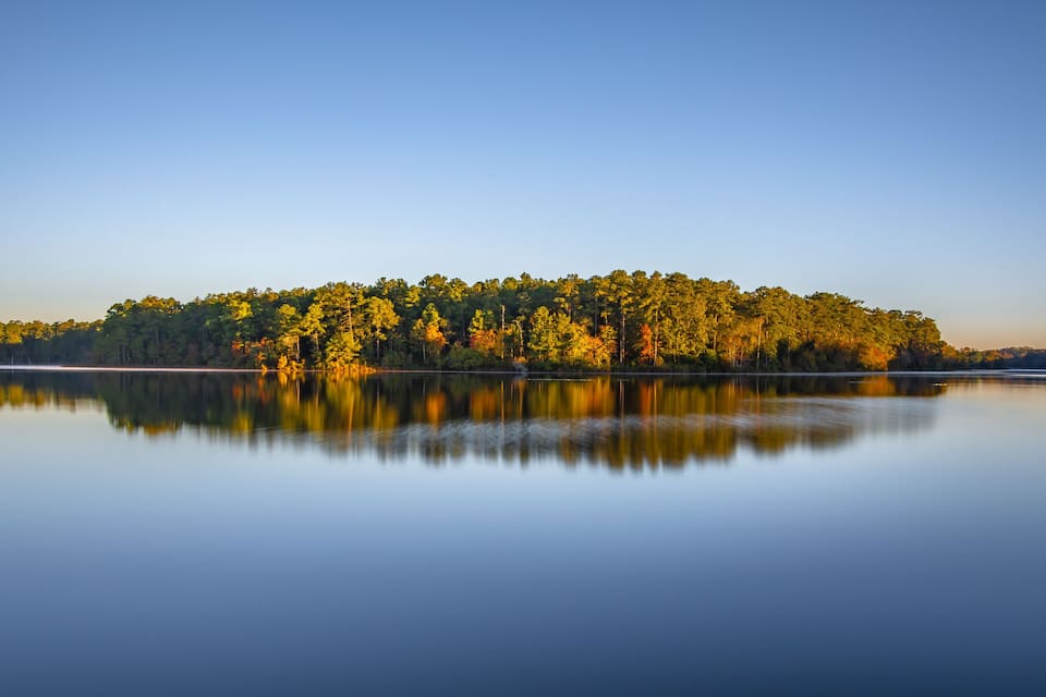 Un lac paisible où se reflète une forêt aux arbres aux couleurs automnales.