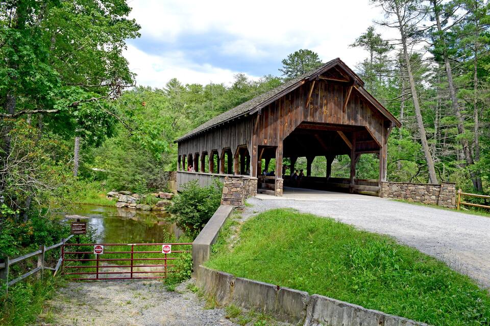 A wooden covered bridge over a small stream in a wooded area.