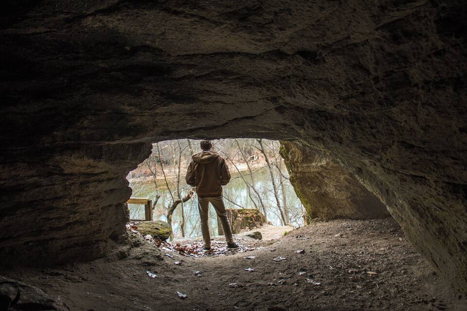 A person standing at the entrance of a cave with a view of a lake.