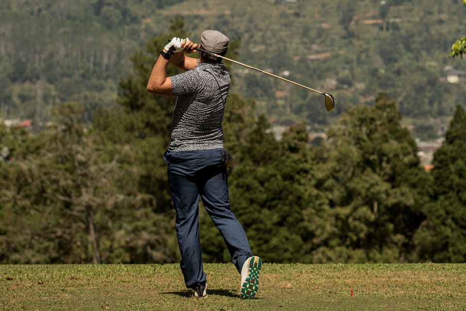 Un golfista a punt de fer un cop en un camp de golf, amb un paisatge ondulat al fons.