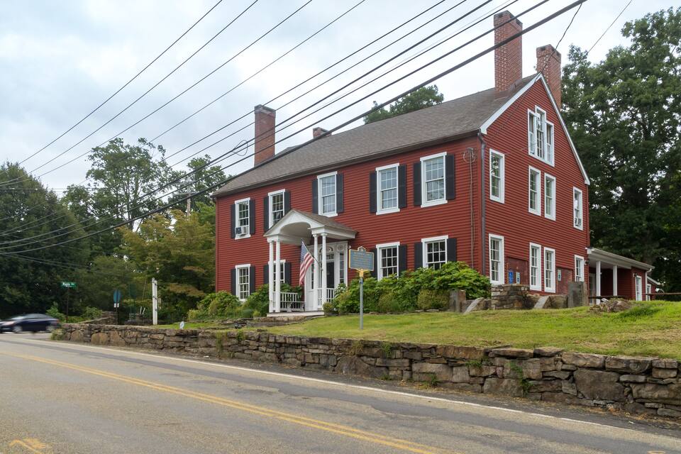 A red colonial house with a white porch and a stone wall in front.