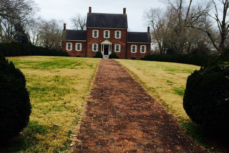 A brick pathway leading to a large brick building with white trim and a central entrance.