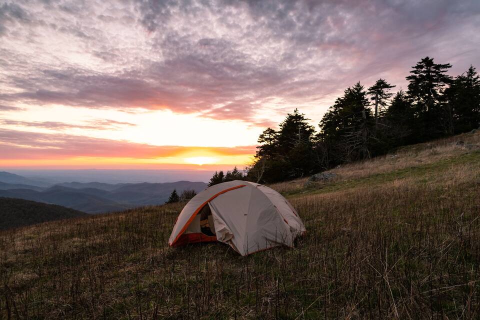Une tente sur une colline herbeuse, avec un coucher de soleil en arrière-plan.