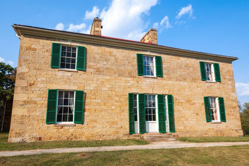 A stone building with green shutters and a white door.