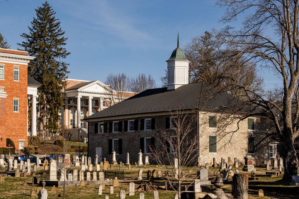 A cemetery with gravestones, a stone building, and a brick building with columns.