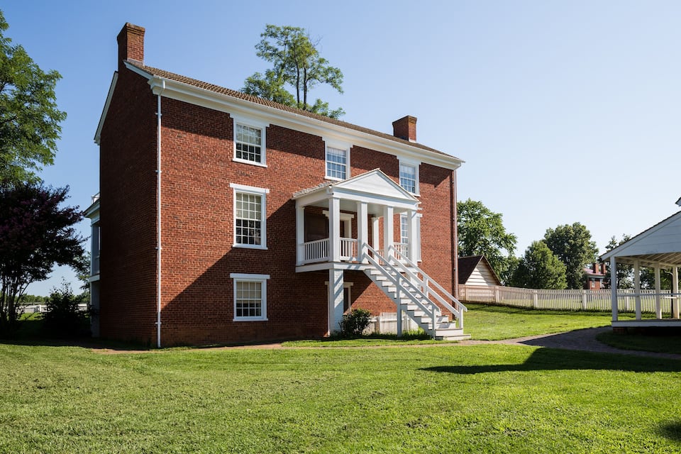 A red brick house with a white porch and a small staircase leading to a balcony.