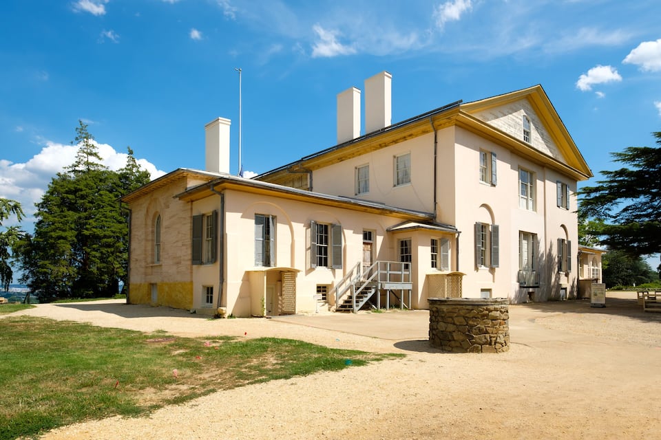 A large, two-story house with a stone foundation, multiple chimneys, and a well-maintained lawn.