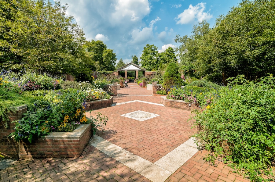 Ein Garten mit einem Gazebo, Ziegelwegen und verschiedenen blühenden Pflanzen.