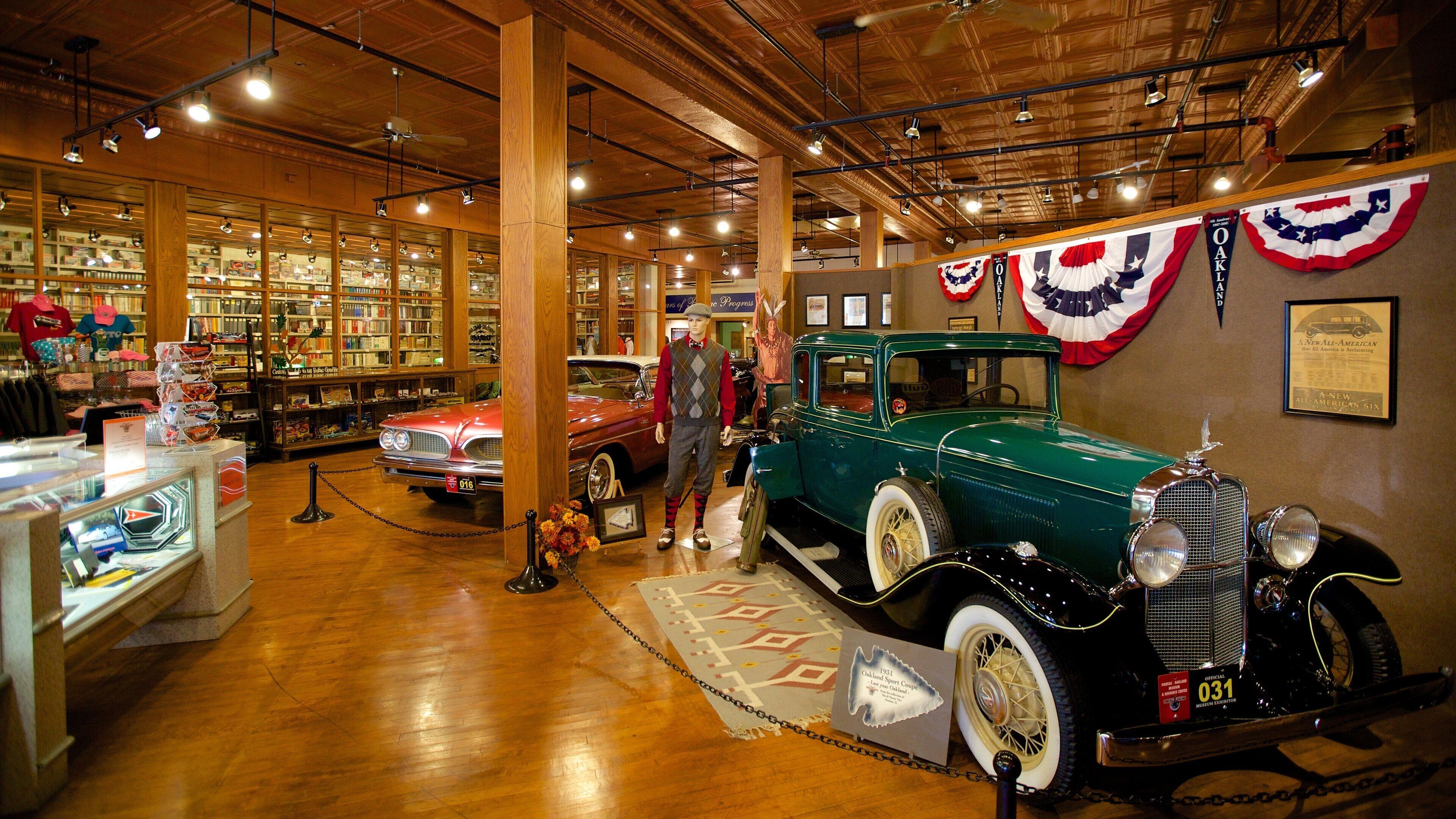 A vintage car exhibit with a green car and a red car on display, surrounded by bookshelves and American flags.
