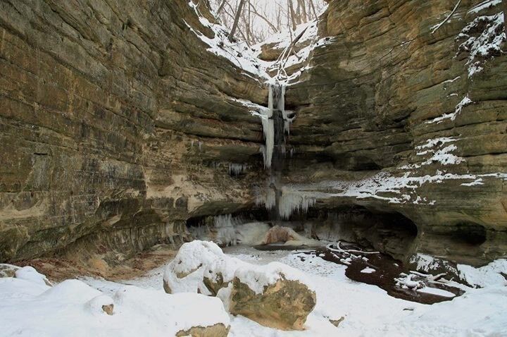 A cave with a waterfall and snow-covered ground.