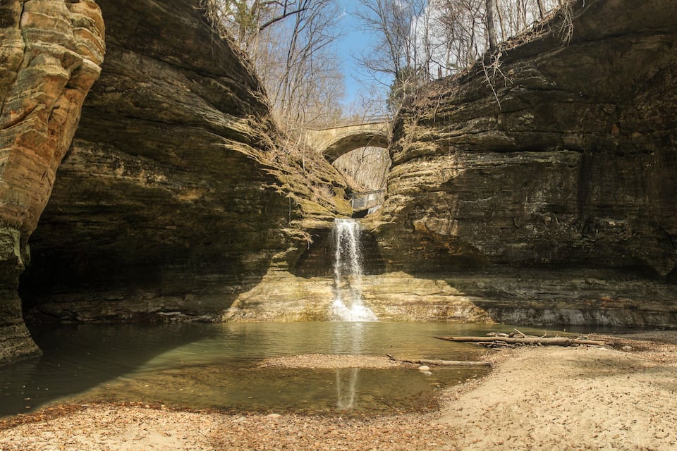 A waterfall in a rocky gorge with a bridge in the background.