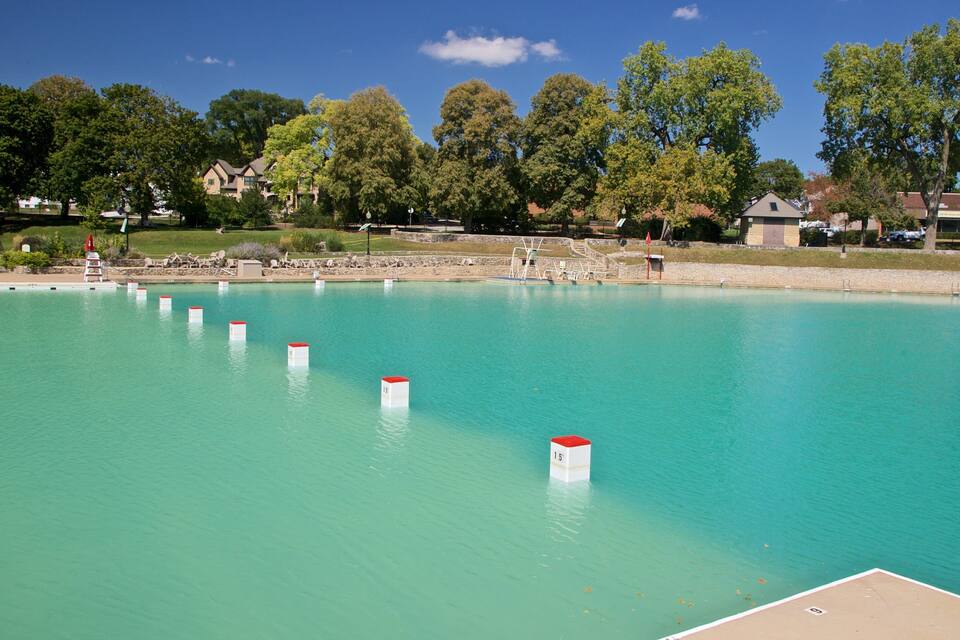 A large swimming pool with clear turquoise water, surrounded by trees and houses.