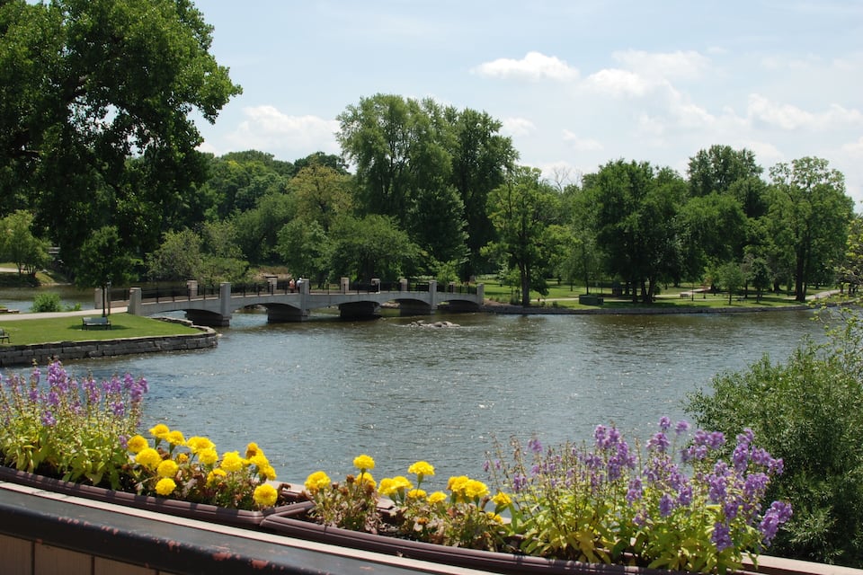 Een rivier met een brug, omringd door bomen en bloemen.