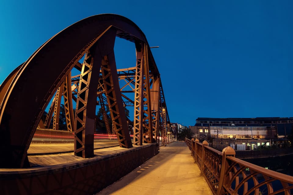 A steel bridge with a curved arch and a concrete walkway.