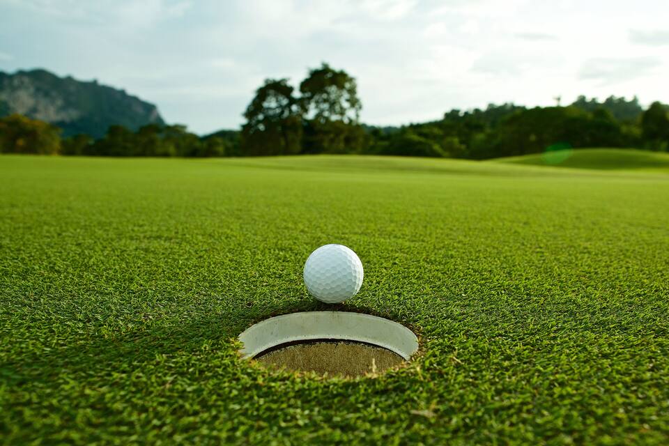 Una pelota de golf sobre un campo de prácticas con un hoyo en el centro.