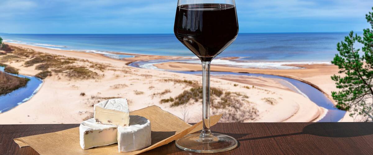 Glass of red wine with brie cheese against view of beach and Baltic see. Beach with white sand, pine tree and blue sea or ocean.