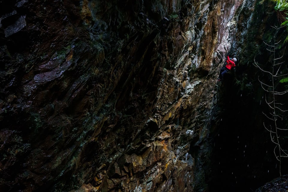 A climber in red climbing a steep, rocky cliff.