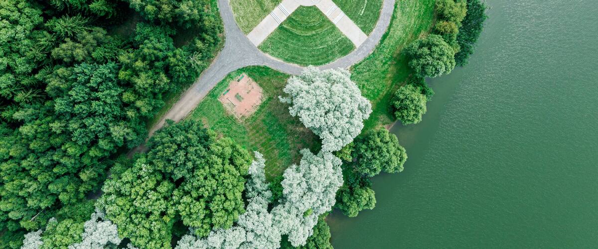 aerial top view from flying drone of a city park with walking path among green trees in sunny day