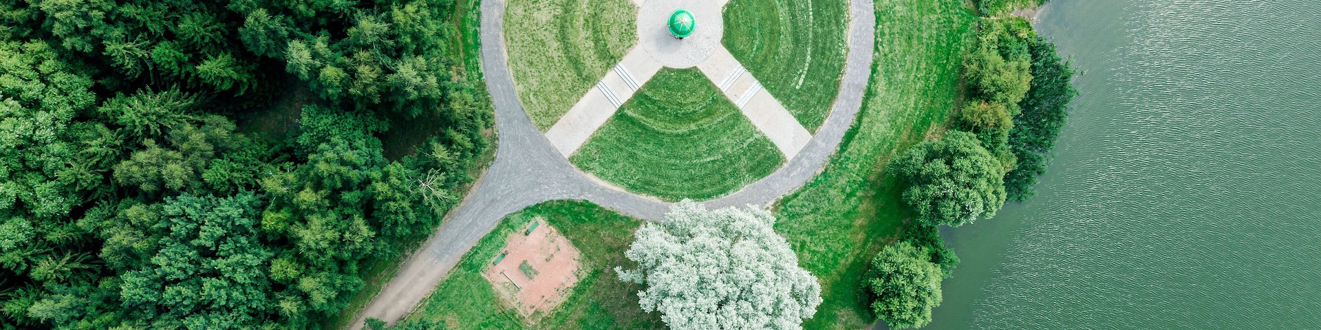 aerial top view from flying drone of a city park with walking path among green trees in sunny day