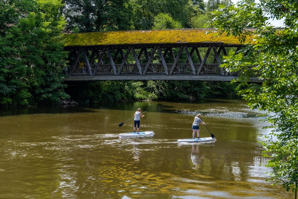 Two people paddleboarding on a river with a bridge in the background.
