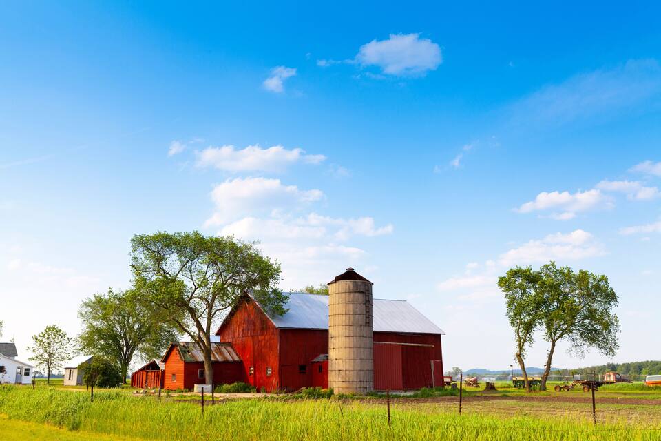 A red barn with a silo, surrounded by green fields and trees.