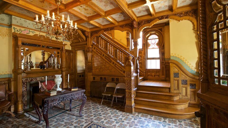 An ornate room with a grand staircase, a chandelier, and a fireplace.