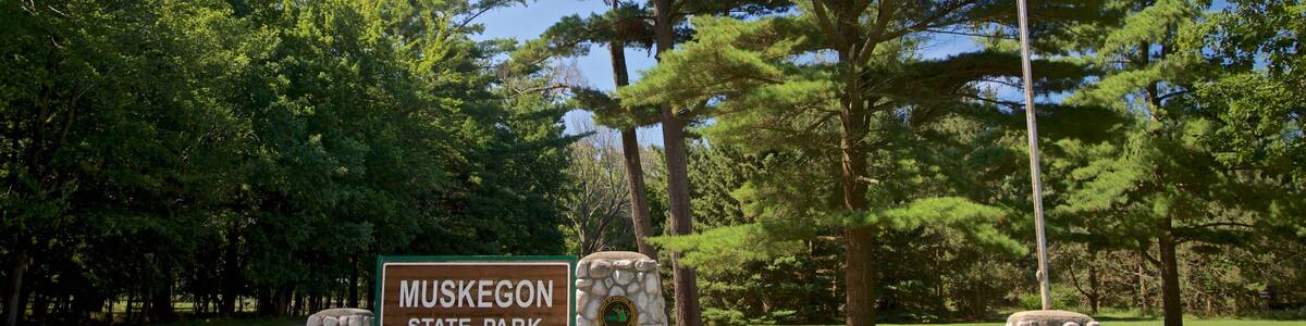 Schild für den Muskogee State Park, umgeben von Bäumen und einer Flagge.