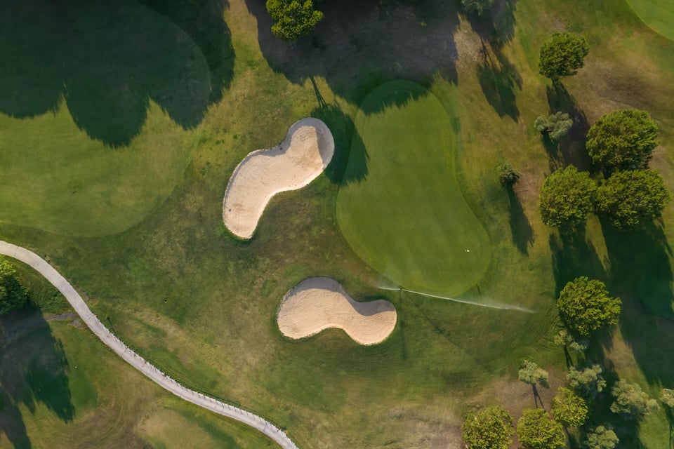 Vista aérea de un campo de golf con búnkeres de arena y un obstáculo acuático.