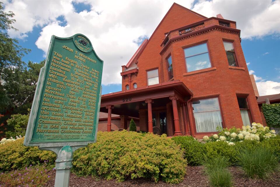 A historic brick house with a green sign detailing its history.