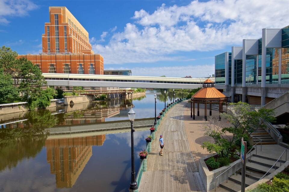 A riverside walkway with a bridge, a modern building, and a gazebo.