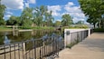 A riverside walkway with a metal railing, trees, and a bridge in the background.