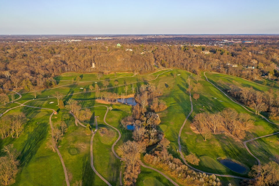 An aerial view of a golf course with multiple greens, water hazards, and a large body of water.