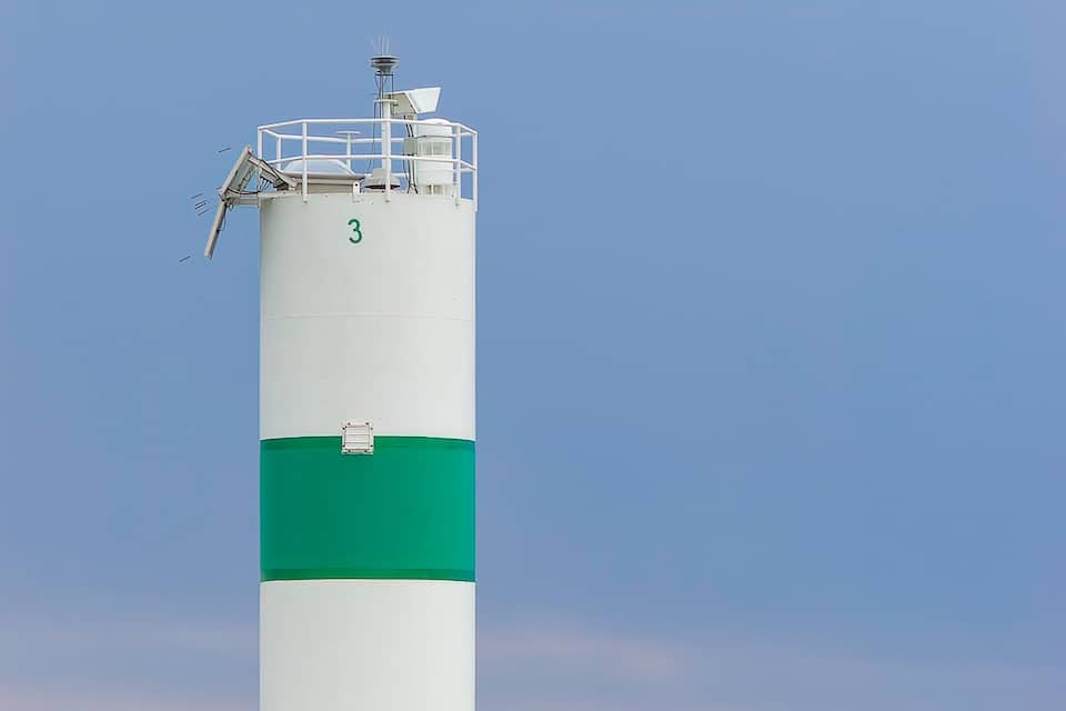 A lighthouse with a green stripe, a wooden pier, and a rocky shoreline.
