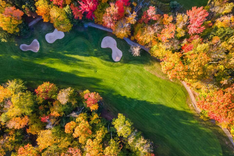 An aerial view of a golf course surrounded by autumn-colored trees.