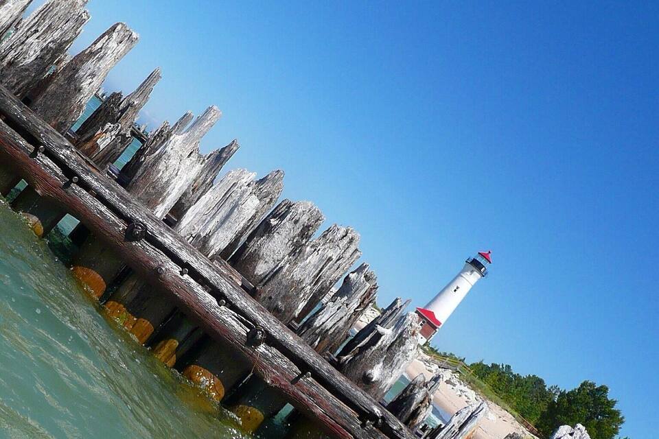 Um farol numa doca desgastada com pintura descascada, rodeado por águas calmas e céu limpo.