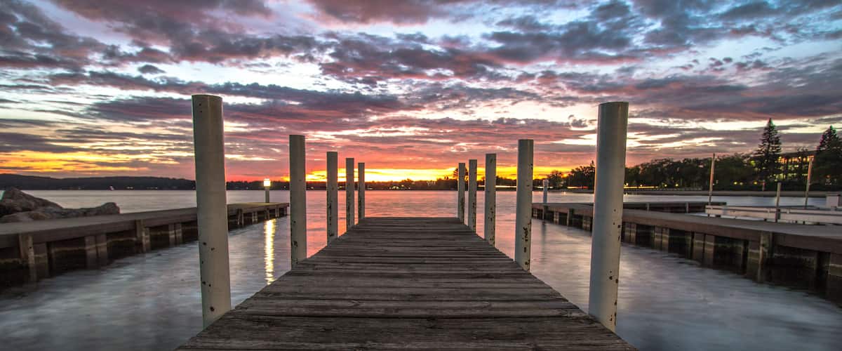 Wooden Dock On Sunrise Lake. Summer sunrise over the waters of Grand Traverse Bay in Traverse City, Michigan. Shot with long wooden dock in foreground sunrise over water at horizon.