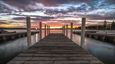 Wooden Dock On Sunrise Lake. Summer sunrise over the waters of Grand Traverse Bay in Traverse City, Michigan. Shot with long wooden dock in foreground sunrise over water at horizon.