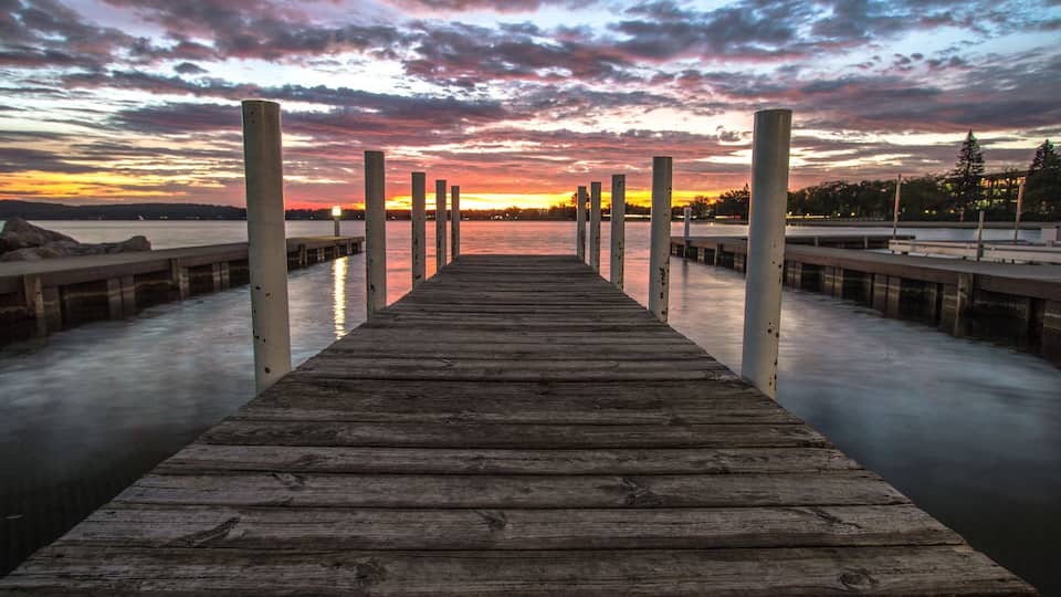 A wooden pier extending into calm water with a sunset sky.