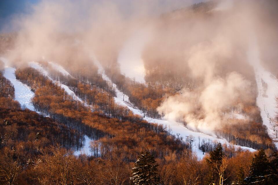 Montaña nevada con un telesilla y humo que se eleva entre los árboles.