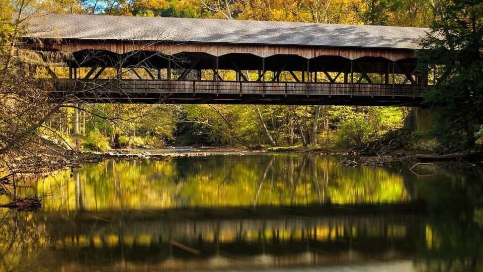 A covered bridge over a calm river surrounded by autumn foliage.