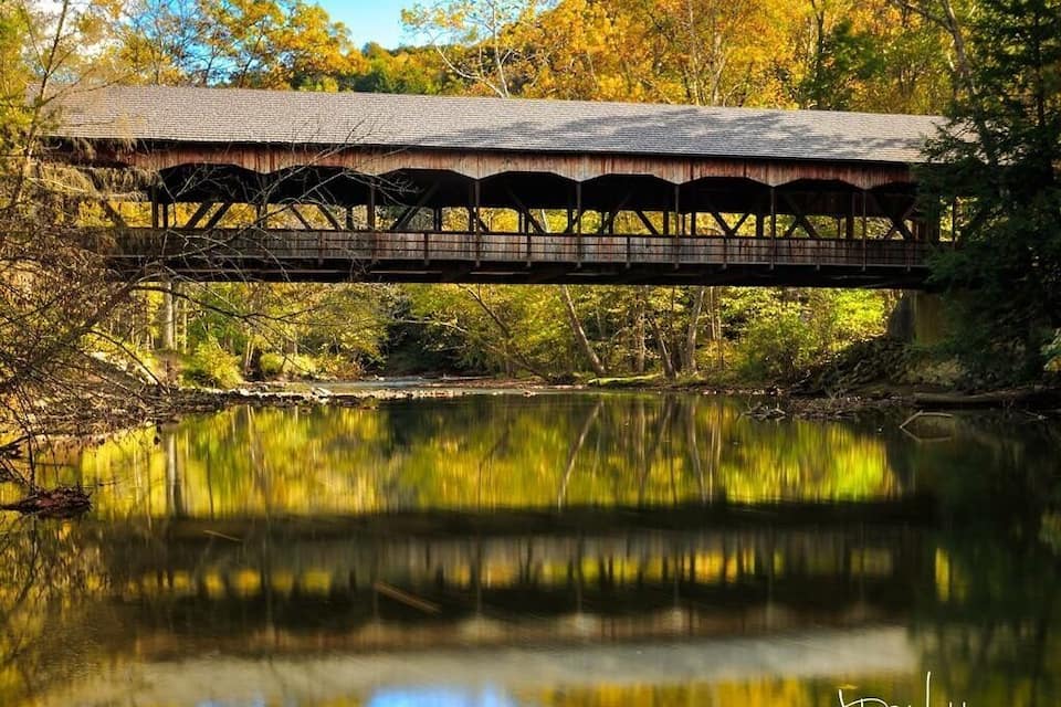 A covered bridge over a calm river surrounded by autumn foliage.