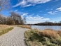 Een grindpad dat leidt naar een bank aan een rivier, omgeven door bomen en grasvelden.