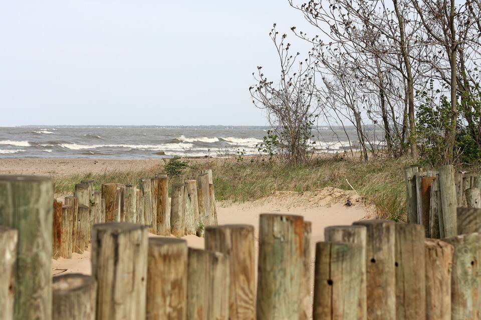 A beach with wooden fences, sandy dunes, and waves crashing onto the shore.
