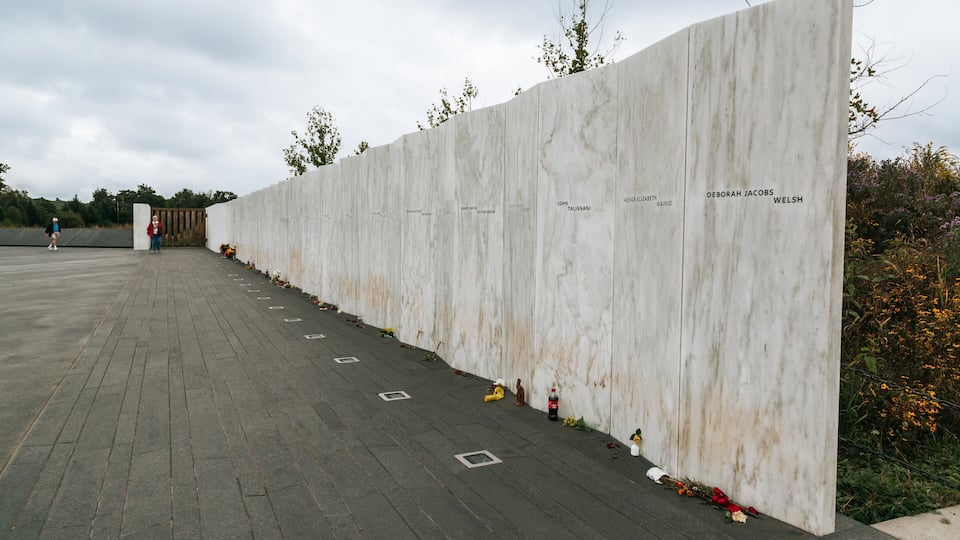 A marble wall with names inscribed, surrounded by flowers and a paved area.