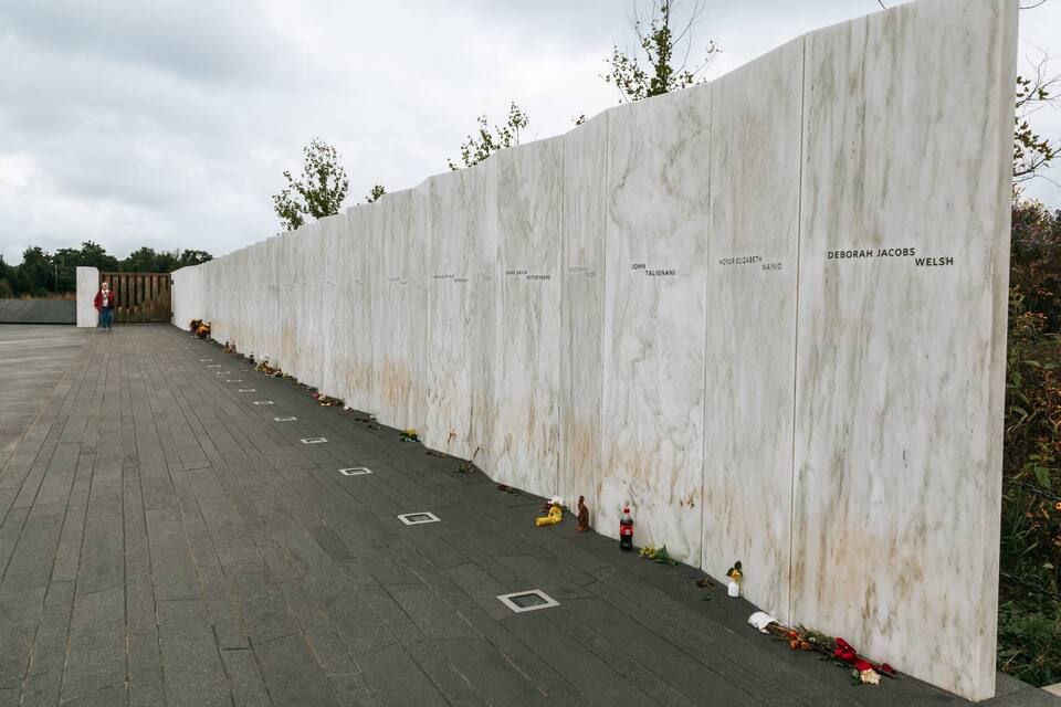 A marble wall with names inscribed, surrounded by flowers and a paved area.