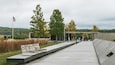 A modern outdoor pavilion with benches, surrounded by trees and a grassy area.