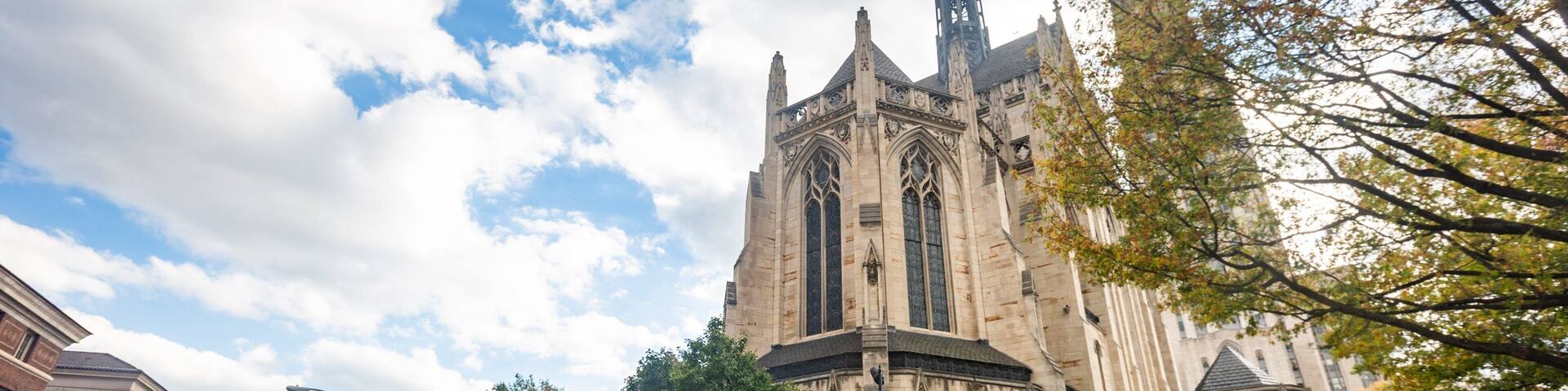 A historic church with Gothic architecture, surrounded by autumn foliage and a city street.