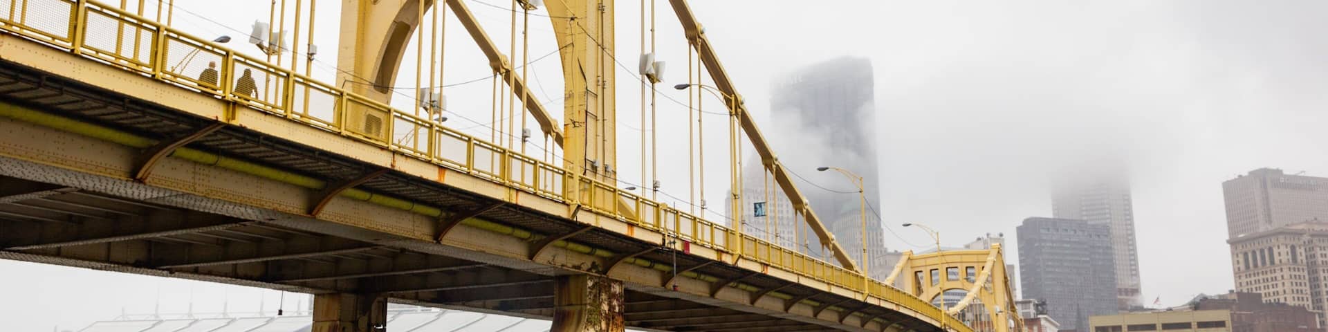 A yellow bridge with a river underneath and tall buildings in the background.